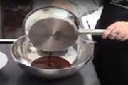 Melted chocolate pouring from a saucepan into a mixing bowl.