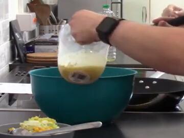 A measuring jug containing liquid being held over a mixing bowl.