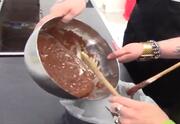 Chocolate mixture being poured into a baking tin and someone holding a wooden spoon.