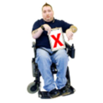 A man in a wheelchair is holding up a clipboard which has a red cross on it