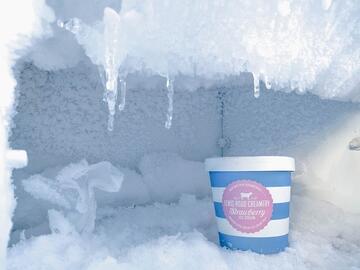 A tub of ice cream in a freezer that has a lot of ice around the sides.