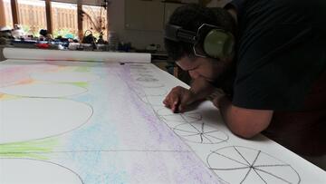 Harvey leaning over a table to colour in his train drawing
