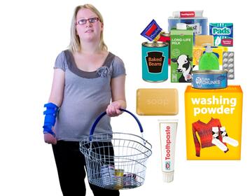 A lady with a shopping basket beside some tins of food, toiletries and washing powder.