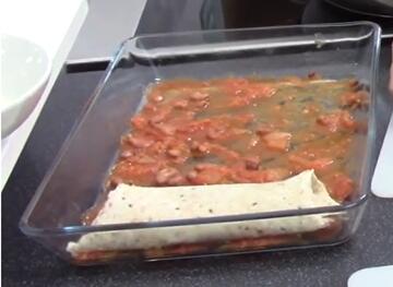 An ovenproof dish with tomato mixture and an enchilada in it.