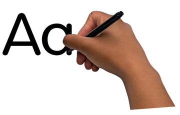 A hand holding a pen next to some black letters.