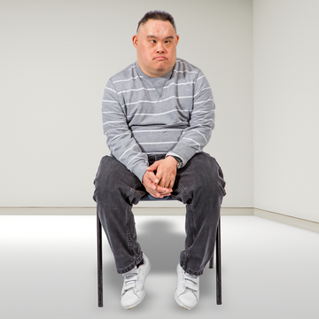 A man is sitting on a chair in a room on his own and he looks sad