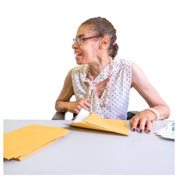 A woman is putting letters in envelopes but has been distracted and is now talking to someone