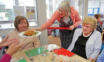 A woman serves food to a table of elderly people.