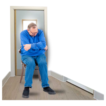A man is sitting in a room on his own with his head lowered and his arms folded.
