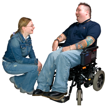 A woman is kneeling down listening to a man in a wheelchair who is talking