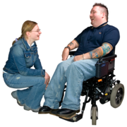 A woman is kneeling down listening to a man in a wheelchair who is talking