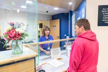 A man is standing at a hospital reception desk talking to a nurse