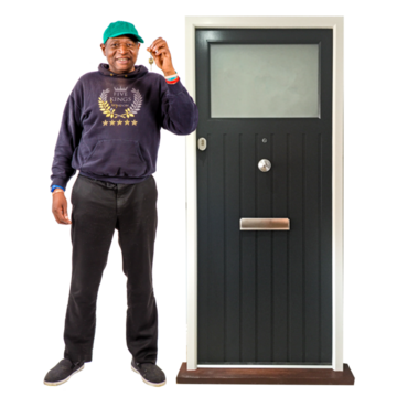 A man in a baseball hat is holding up some house keys next to a front door