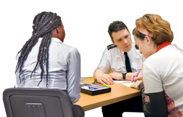 A supporter is sitting next to the person talking to the policeman at a desk in a meeting room