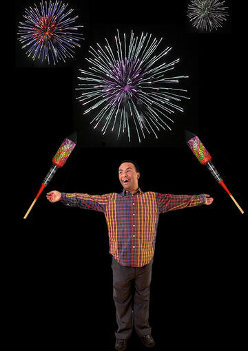 A man standing with his arms stretched out with fireworks in the background