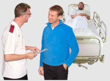 A nurse talking to a smiling friend of a man who is in a hospital bed behind them listening to their conversation