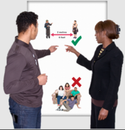 Two managers either side of a flip chart pointing to a picture of safe distancing with a green cross on it. Below that is a picture of several people on and around a sofa with a red cross next to it.