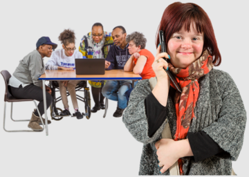 A woman on the phone in the foreground. Behind her is a group of people at a table huddled around a laptop listening to her call.