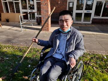 A man in a wheelchair smiling and holding a rake