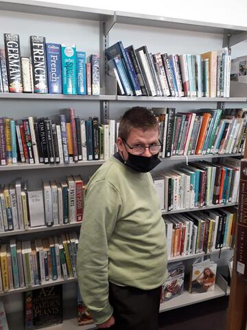 A man standing against a bookcase with lots of books