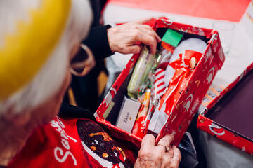 An elderly person opens a shoe box that has been wrapped and filled with gifts by people from Tameside Me Time 