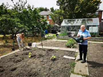 A man standing in an allotment holding a watering can
