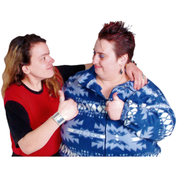 Two women have their arms round each others shoulders and hold thumbs up