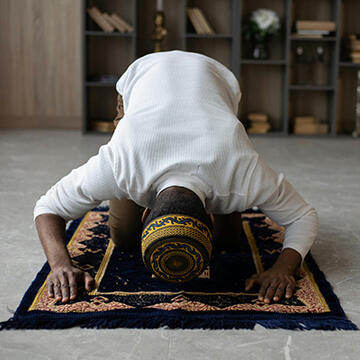 A Muslim man on his knees praying on a prayer mat.
