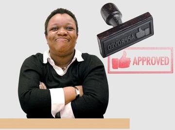 A woman with her arms folded on a table smiling, with an approved stamp next to her