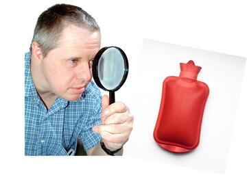 A man looking through a magnifying glass at a hot water bottle.