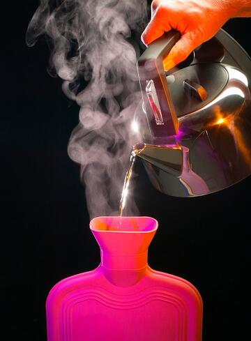 Someone pouring hot water from a kettle into a hot water bottle.
