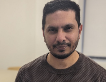 Ismail has short dark hair and beard, and is wearing a brown top.
