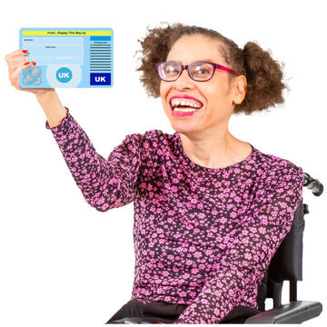 A lady in a wheelchair holding up a Blue Badge and smiling.