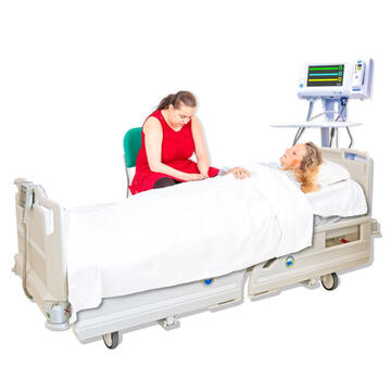 A lady sitting beside a hospital bed and looking sad because the person in the bed has died.