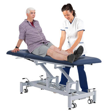 A man sitting on a couch with a physiotherapist looking at his leg.