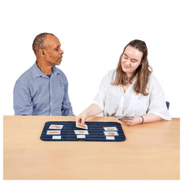 2 people sitting at a table.  On the table is a mat with picture cards on it.