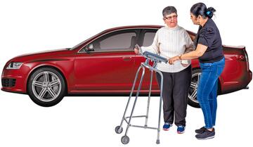 A lady helping a lady with a walking frame by a car.