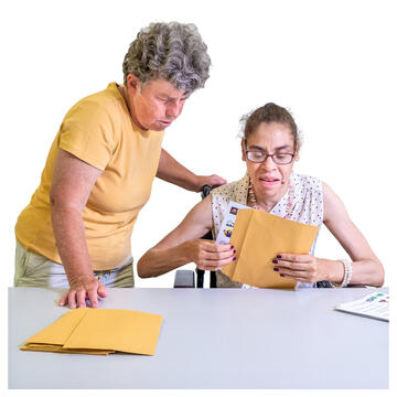 Two ladies at a table.  One lady is putting some paper into an envelope.
