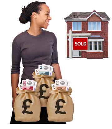 A woman smiling with some bags of money beside her.  She is looking at a house which has a sold sign outside it.