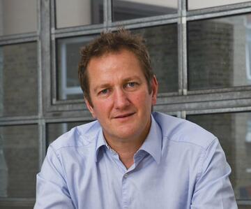 A man in a blue shirt with short dark hair looking at the camera