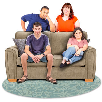 Two people sitting on a sofa with 2 other people standing behind the sofa.  They are all smiling and looking happy.