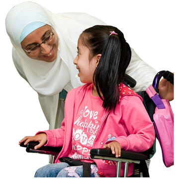 A woman smiling and looking at a girl in a wheelchair