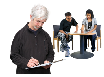 A man in the foreground signing a piece of paper on a clipboard. Two people are behind him at a table also signing a piece of paper.