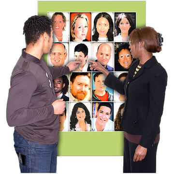 A man and a lady standing in front of a board with pictures of lots of faces on it.  They are both pointing to the same face on the board.