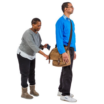 A woman reaching towards a man's satchel without him knowing.