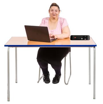 A woman sitting at a table typing at a laptop with a mobile phone beside her.