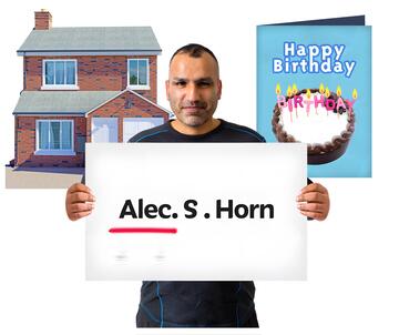 A man holding up a card with his name on it.  Behind him is a house and a birthday card.