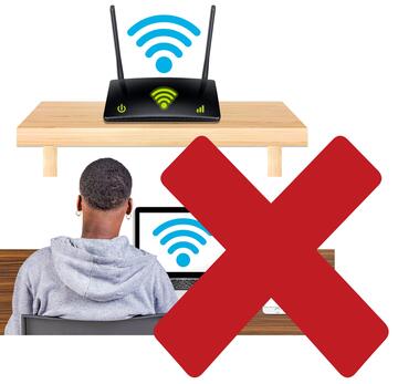 A man sitting at a laptop with his phone beside him.  The laptop and the phone have a wifi signal.  There is also a router with wifi signal.