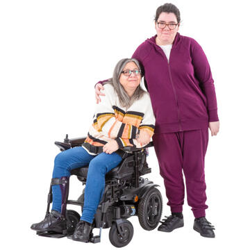A woman standing beside an older woman who is in a wheelchair and has her arm around her.