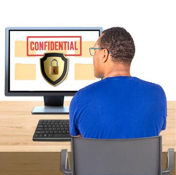 A man sitting at a laptop which has an image of a shield and a padlock and the word confidential on the screen.